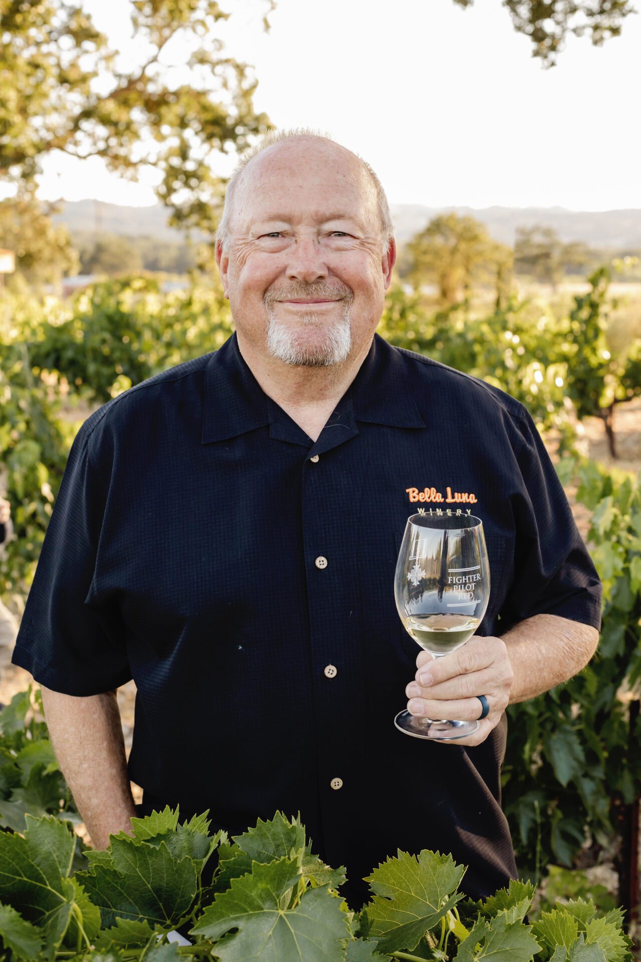 Sherman Smoot, co-founder of Bella Luna Estate Winery, holding a glass of wine amidst the vineyard in Templeton, California.